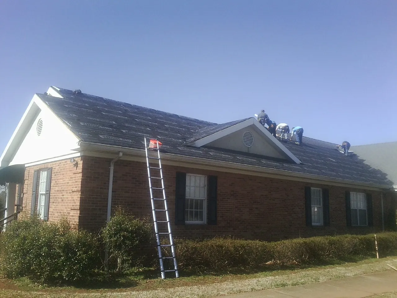 Crew tearing shingles off a brick ranch roof with a ladder set — Metal Roof Repair work by our crew in San Geronimo