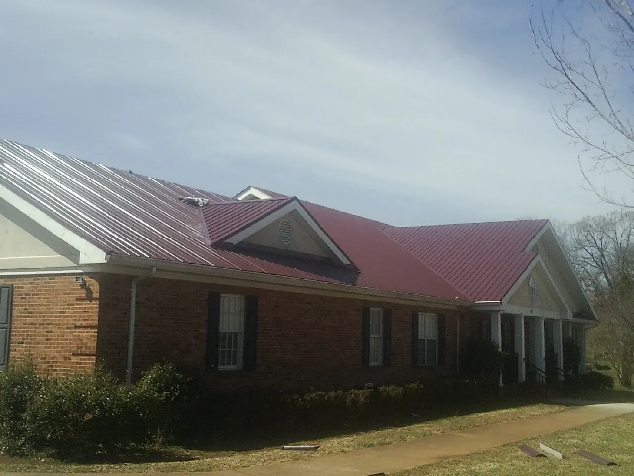 Red metal roof with gabled entries on a long brick building, from a Hail Damage Roof Repair job in San Geronimo