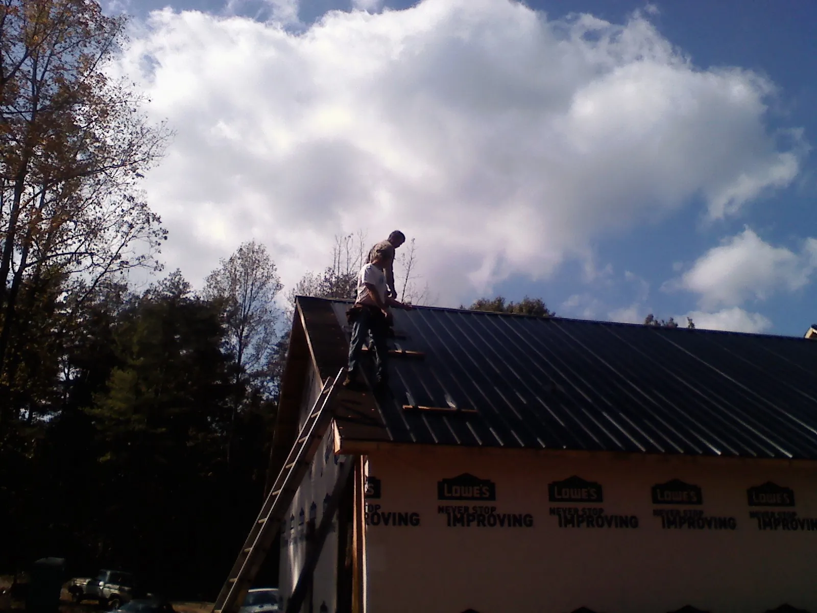 Roofer fastening dark metal panels high against a cloudy sky, from a Roof Inspection job in San Geronimo