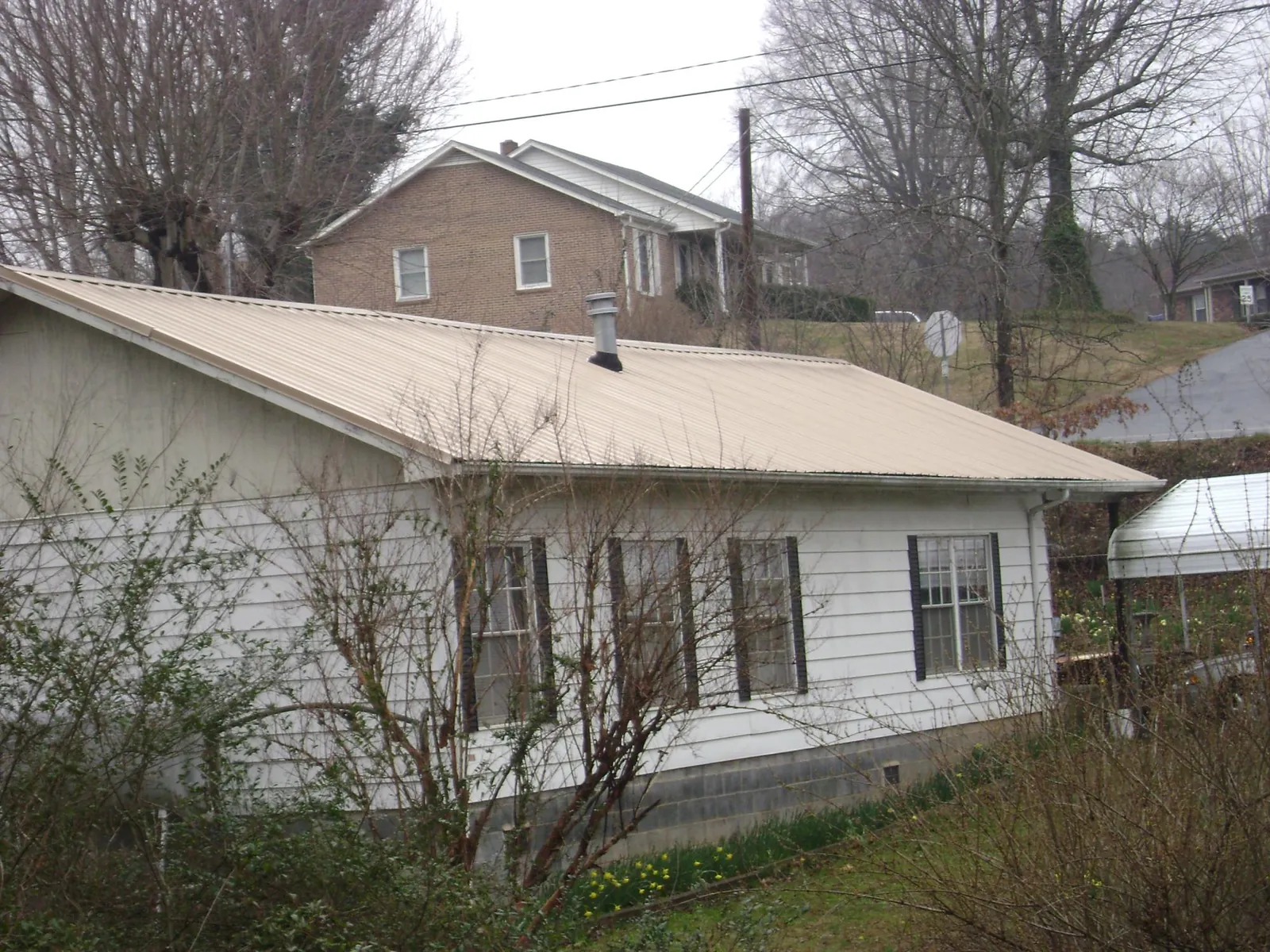Tan metal roof on a white sided house set into a hillside — Commercial Roofing by Roofing Brothers in San Geronimo